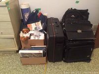 Image showing multiple luggage including a large Delsey suitcase, an APC backpack, a navy airline bag, a small teddy bear, and boxes containing various airline swag items such as postcards and books.
