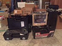 Multiple sets of Campbell cable tire chains in cases and original packaging on a floor with boxes in background.