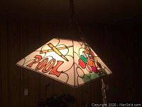 Plastic Tiffany-style pool table lamp showing decorative graphics of pool cues, billiard balls, and the word 'POOL' on a stained glass-like plastic surface.