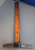 Front view showing the wooden ruler with black measurement markings and attached metal perpendicular arm with patina.