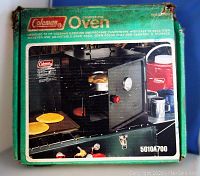 Front of the original green cardboard box showing image of the fold-away oven in use on a camping stove, with food baking inside the oven.