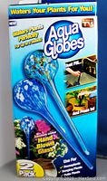 Front view of original packaging with two Aqua Globes inside, showing product name, features and hand blown glass design.