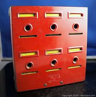 Front view showing six slots and holes for inserting money. Red metal exterior with yellow interior boxes visible through slots.