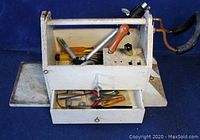 Front view of vintage handmade wooden toolbox showing contents including screwdrivers, hammer, and hand-crank drill, with lower drawer open revealing additional hand tools.