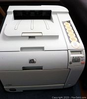 Front view of HP Color LaserJet CP2025dn printer showing top paper output tray, control buttons, and status indicator panel.