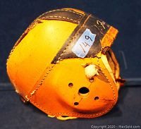 Side view with visible damage to leather exterior, with worn spots and tears in yellow leather, stitching details and chin strap shown.