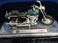 Front side view of the Maisto die cast motorcycle model in metallic teal and chrome detailing on display base showing Harley Davidson logo and model name.