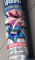 Close-up of kite packaging showing SpinBox Rotating Box Kite branding with geometric kite image, ripstop nylon, pop up assembly, fiberglass airframe