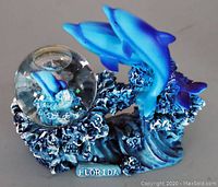 Close-up of dolphin snow globe showing two dolphins leaping above ocean waves with coral base and 'FLORIDA' metal plaque