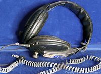 Photo of black padded over-ear headphone showing ear cup and coiled audio cord with 3.5mm jack plug