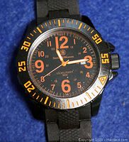 Close-up of watch face showing black dial, orange numerals, Smith & Wesson logo and US Military text.