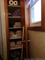 Linen cupboard with shelves containing towels, paper products, and cleaning items; a dust mop resting against door