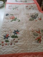Full view of quilt showing white background with multicolored floral prints and peach border.