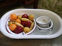 White enamelware tub filled with assorted plastic fruit and enamel bowls stacked inside.