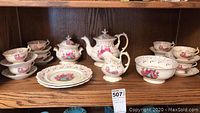 Full set arranged on wooden shelf showing teapot, cream pitcher, sugar bowl, serving bowl, cake plates, cups and saucers.