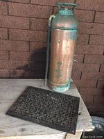 Fire extinguisher and floor grate on wooden surface against wall.