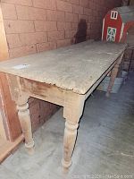 Side view of vintage wooden work table showing plank top and turned legs with worn and damaged surface.