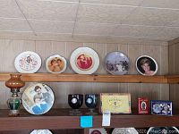 Five Royal Family themed commemorative plates on a wooden shelf; each plate shows different portraits including Princess Diana and Prince Charles.
