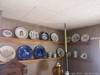 Plates and cups arranged on two wooden plate rails on paneled wall, showing full lot display