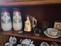 Wide shelf view showing all collectible royal commemorative items including vases, figurine, pin cushion, teacup, mug, and framed portrait.