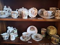 Two wooden shelves with various porcelain royal memorabilia items including teapots, cups, saucers, and plates featuring Queen Elizabeth II images and royal crests