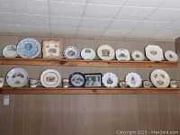 View of two wooden plate rails displaying 23 commemorative plates and mugs along with a framed photo beneath the lower rail.