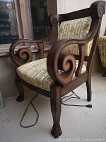 Side view of the armchair showing the scrolled wood arms and claw foot front leg, floral striped upholstery on seat and back.