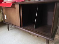 Front view of walnut record cabinet with sliding doors partially open showing the upright dividers inside for record storage.