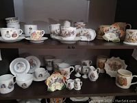 Two shelves filled with various porcelain cups, saucers, plates, and small pitchers depicting British royalty such as Edward VII, George V, and Queen Elizabeth II. Items arranged to show multiple items in one photo.
