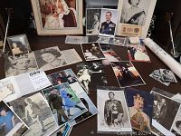Wide view of table surface covered with multiple postcards and photographs of British Royal Family, including Queen Elizabeth II and other members in various poses and attire. Mix of black and white and color images.