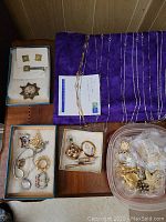 Various costume jewelry pieces including chains, pins, earrings, bracelets laid out on a table with purple fabric underneath.
