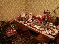 Wide view of table and adjacent chair covered in Christmas decorations including figurines, mugs, reindeer, nutcracker, candles, small trees, and other ornaments.