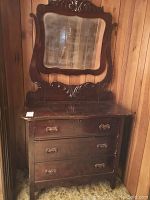 Full view of wood dresser with attached carved mirror showing scalloped front and three drawers with decorative handles. Wear and scratches visible on surface.