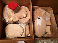 Two boxes filled with stacked oval and various shaped wood plaques, some wrapped in plastic and secured with tape, plus a container with metal hooks.