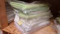 Stack of green and white folded tablecloths wrapped in plastic on wooden shelf.