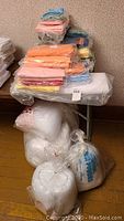 Photo of a large pile of folded quilting fabric in pastel and bright colors stacked on a table, with several large bags of white batting on the floor beneath.