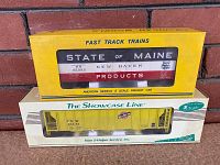 Two boxed S scale train cars stacked, showing the yellow State of Maine box and the yellow gondola car in clear display window box below.