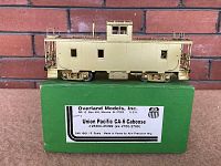 Side view of unpainted brass caboose seated on original green Overland Models box. Label shows Overland Models, Inc., Union Pacific CA-6 Caboose #25300-25399, S Scale, made in Korea by Ajin Precision.