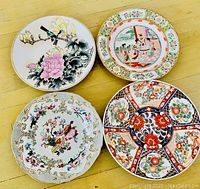 Photo of four collectible fine china plates with varied hand-painted designs including flowers and figures.
