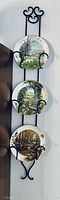Three porcelain collectible plates displayed vertically on a black metal rack against a white wall, showcasing seasonal countryside artwork.