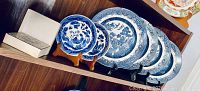 Four large blue and white Churchill England Willow plates paired with two smaller decorative plates, displayed on wooden shelves with plate stands.