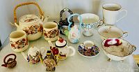 Full collection of assorted hand-painted ceramic teapots, cups, and tea sets on white surface showing variety of styles and sizes.