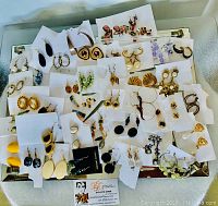 Top-down view of assorted women's earrings on white cards, various styles, colors, and shapes visible