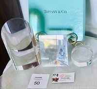 Three clear crystal Tiffany & Co. paperweights with a Tiffany branded clear stand behind them displaying the items together for the lot.