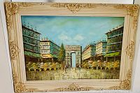 Front view of painting showing a street scene with a white archway between two large buildings and flower beds, ornate cream frame visible