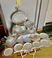 Full assortment of china displayed on white table covering, showing serving platters, bowls, plates, sugar bowl and creamer with floral and gold decoration