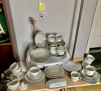 Wide view of the full china set on tables showing plates, cups, saucers, serving pieces with Wheat Harvest floral and wheat motif in soft blue and gold trim