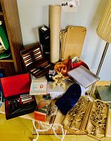 Overview of assorted household items grouped on floor including lamp shade, wooden chess set, red cushioned seat, decorative metal panels, wooden candle holders, and other small items.