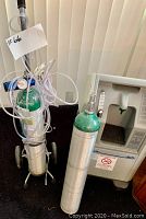 Two oxygen tanks, one with pressure gauge and tubing on a wheeled cart, next to a portable oxygen concentrator.