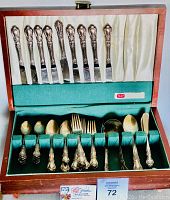 Complete set of silverware in wooden case with separate compartments covered by white and green fabric.